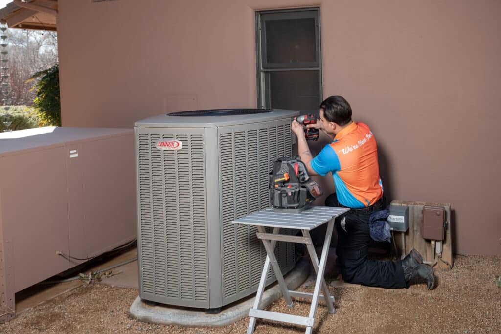 HVAC technician repairing an outdoor air conditioning condenser unit beside a home